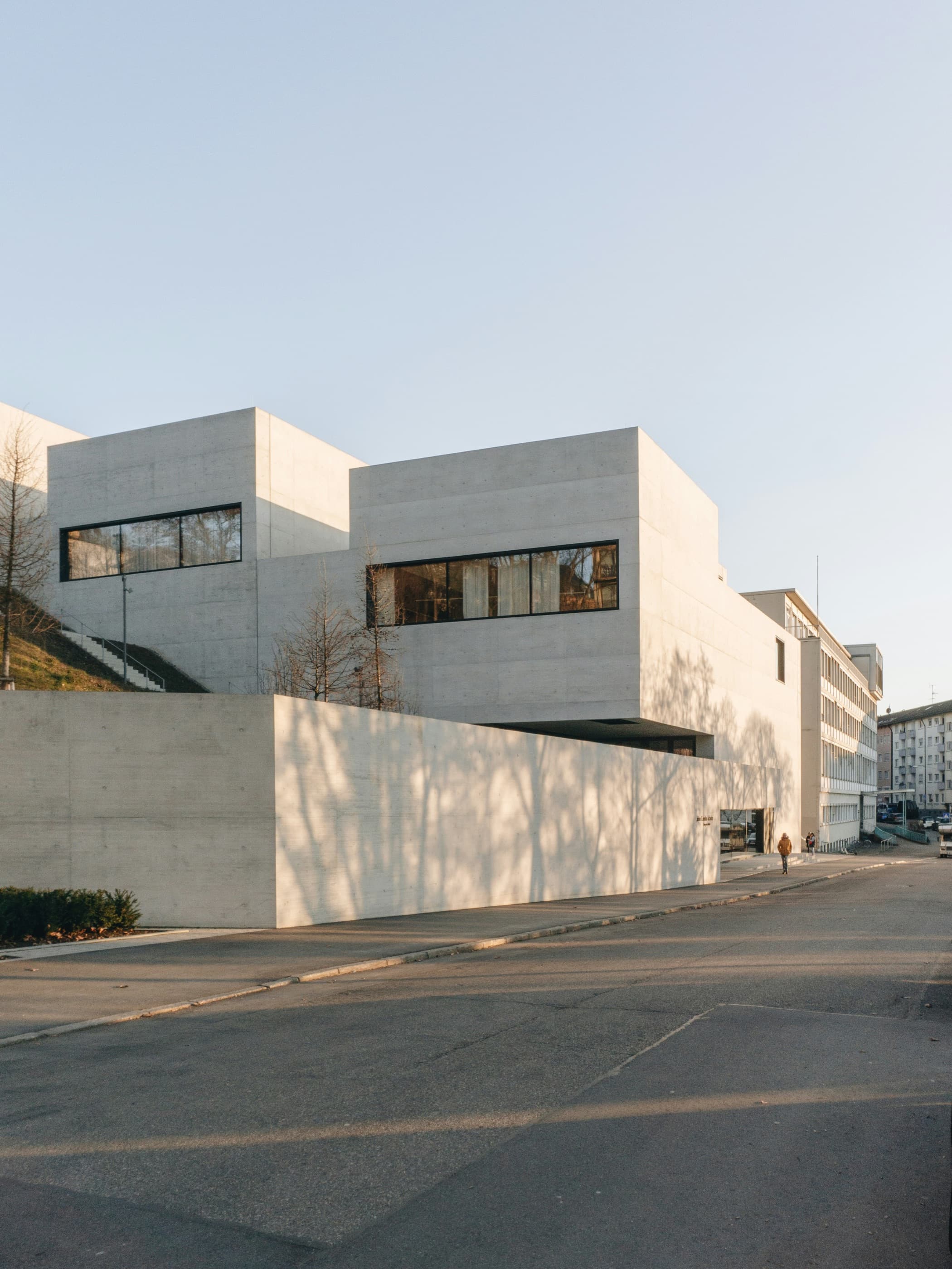 A pale concrete arts building in low golden light, seen across an empty street