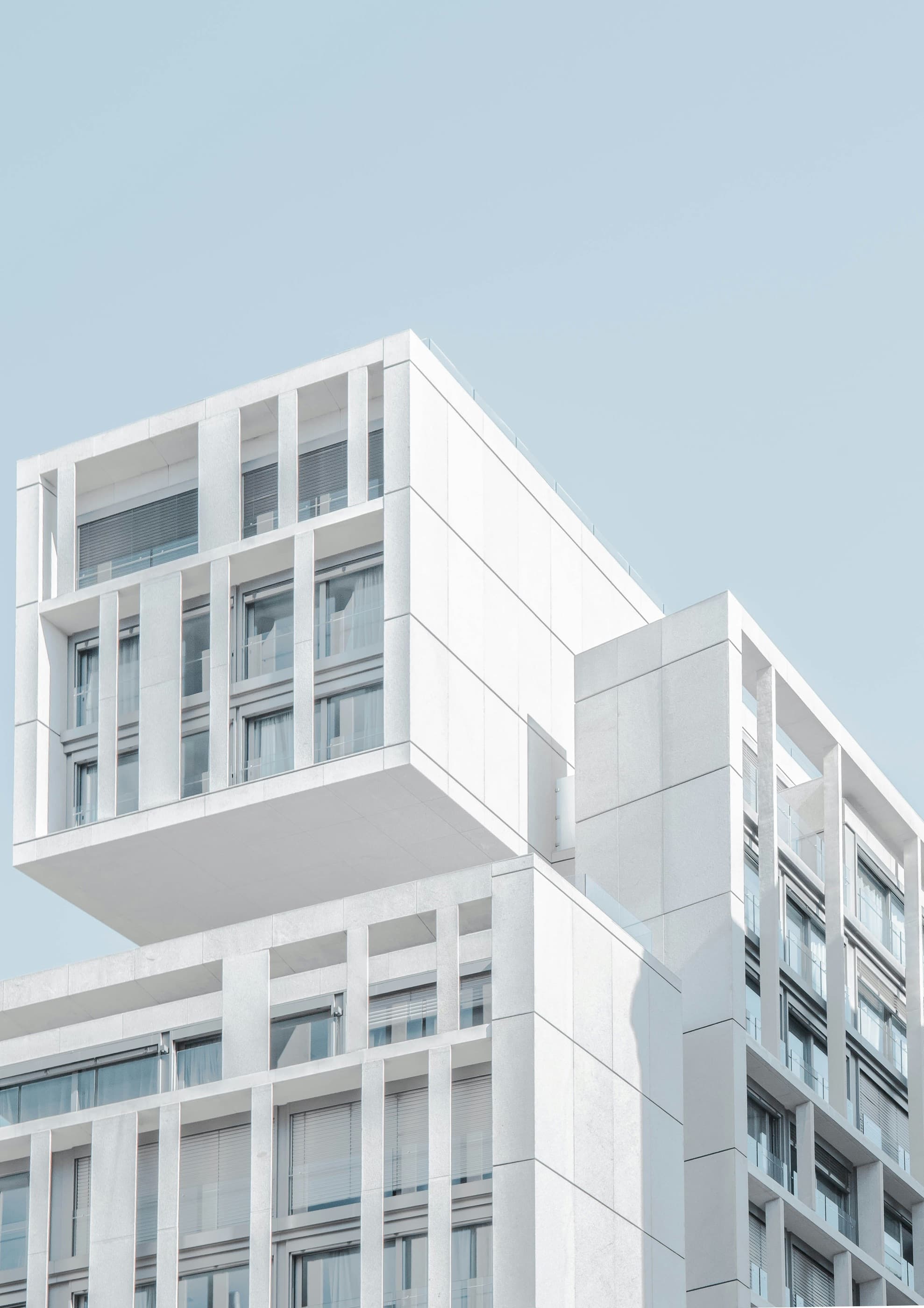 A white modernist building with a cantilevered upper volume against a pale blue sky